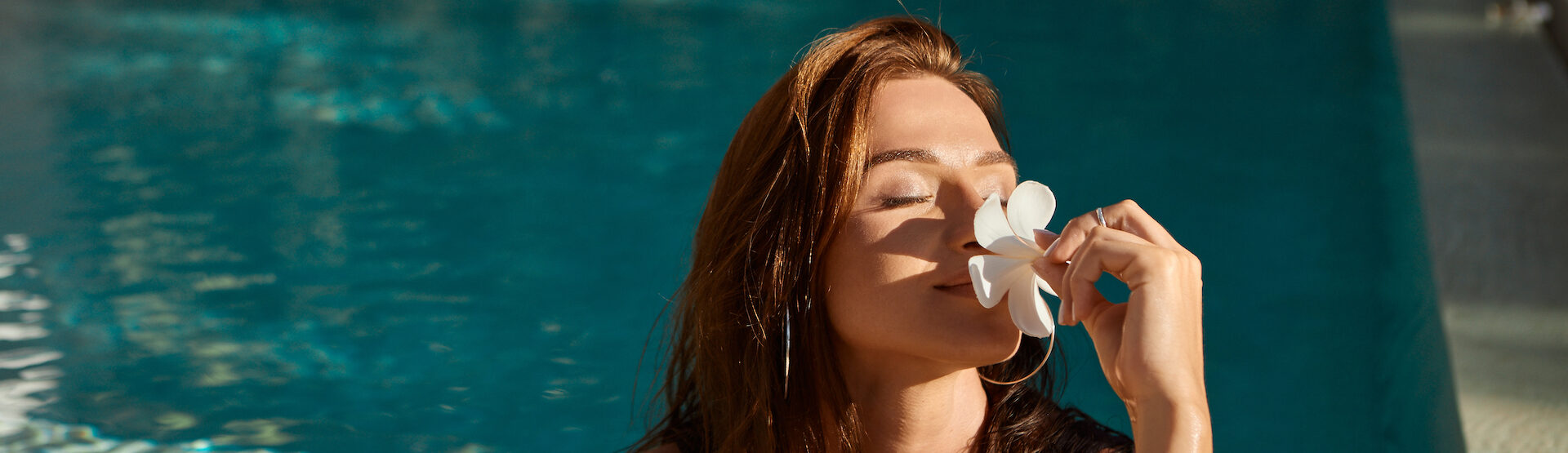 Woman with flower in her hand relaxing in outdoor swimming pool in Bali luxury resort. Beautiful young woman smell  flowers at swimming pool