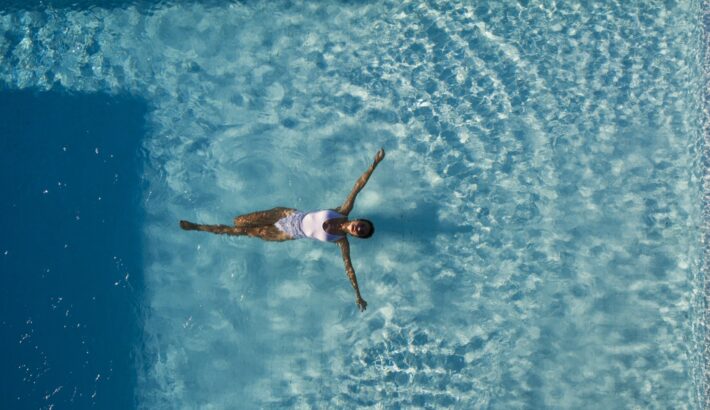 Top view aerial photo from flying drone of a seductive sexy model in white swimwear is enjoying relax in hotel pool during her summer weekend. Amazing fashion woman in bikini having luxury spa rest