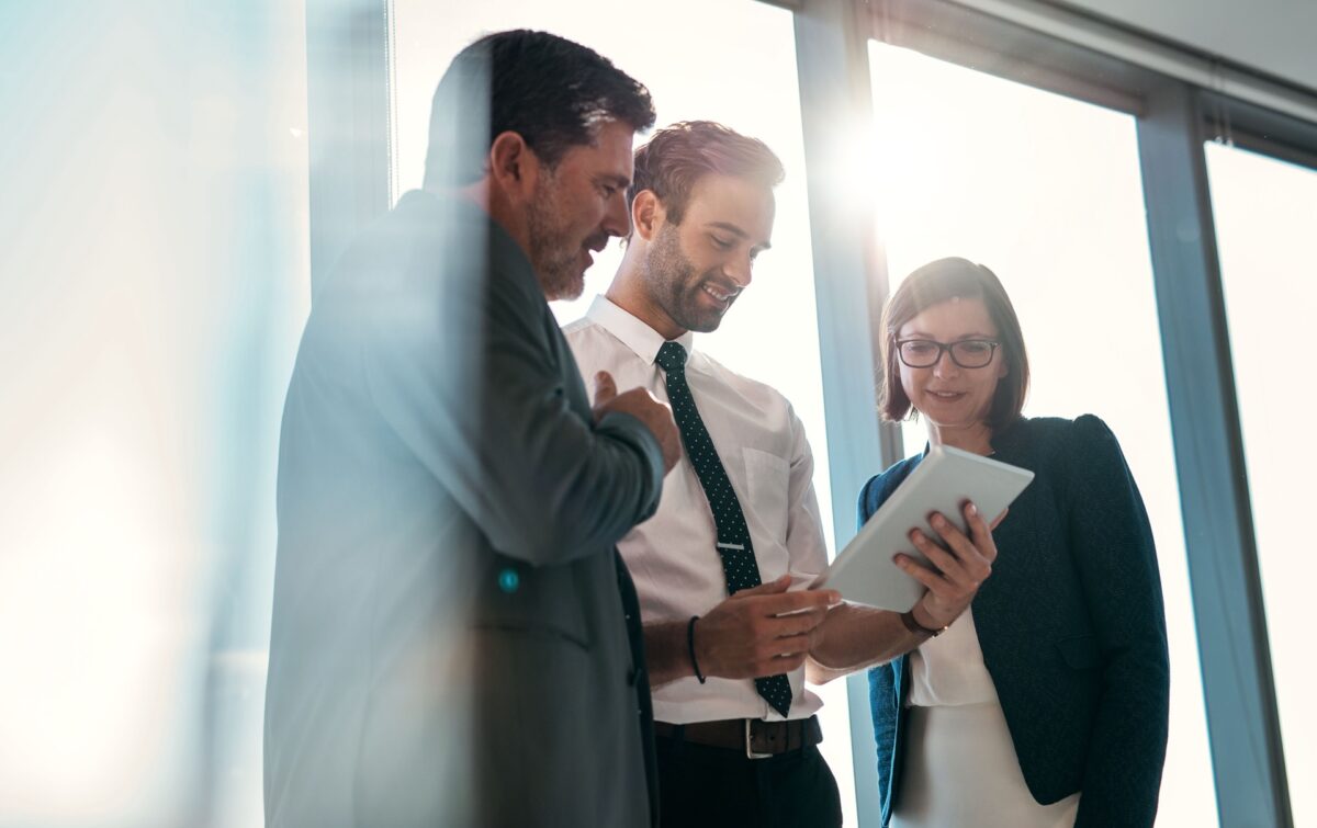 Group of businesspeople using a digital tablet together in front of office building windows overlooking the city