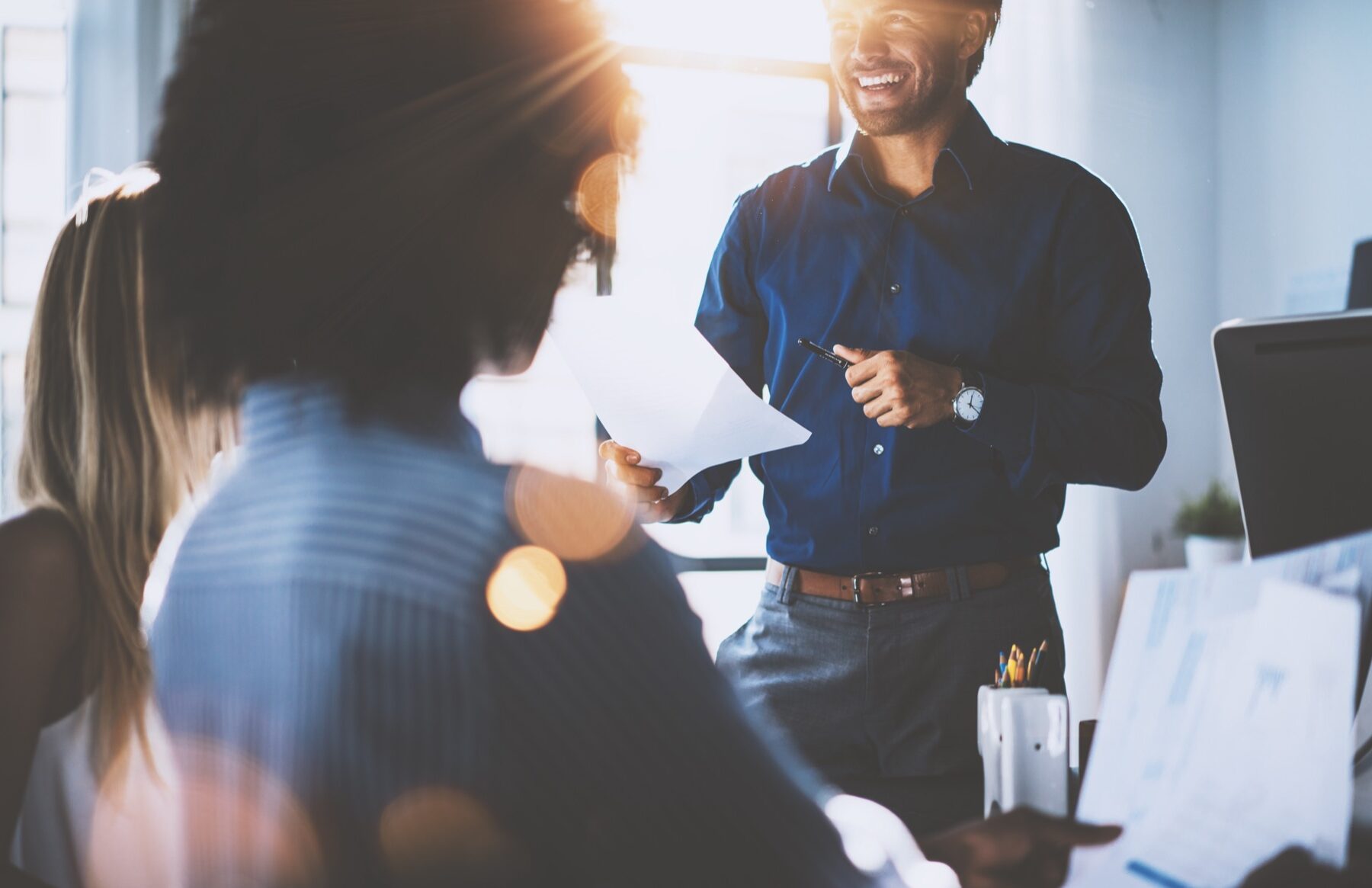 Hispanic businessman holding papers hands and smiling.Young team of coworkers making great business discussion in modern coworking office.Teamwork people concept.Horizontal, blurred background, flares